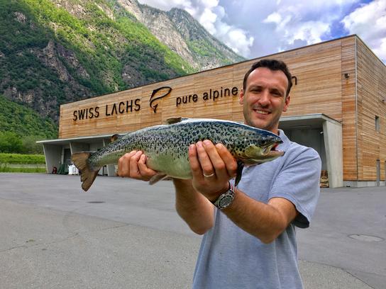 Man with a fish in front of the Swiss Alpine Fish plant 